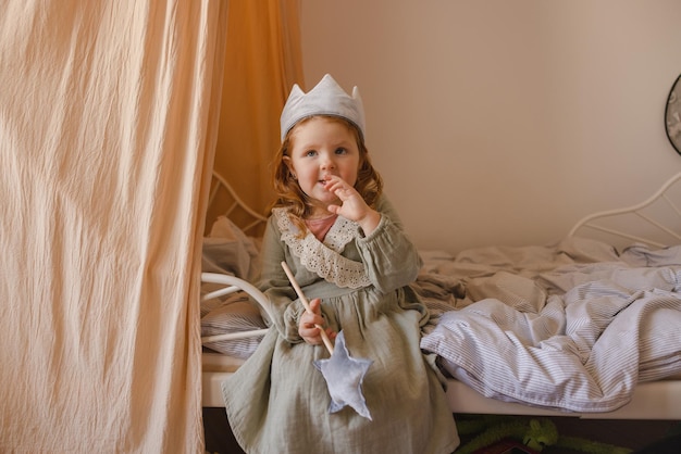 Free photo little caucasian redhaired baby in dress plays princess while sitting on bed in children's room toddler concept