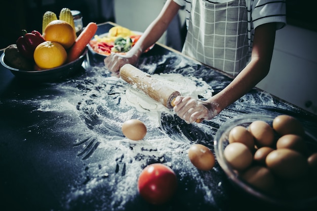 Маленький шеф-повар, используя скалку, растягивая тесто. Концепция приготовления.