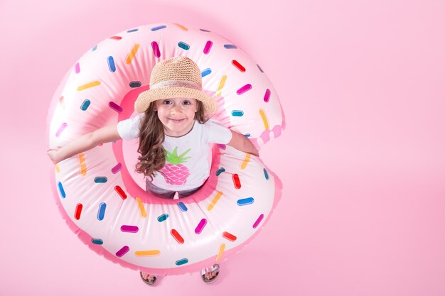 Маленькая девочка в повседневной одежде, лежа на круге надувной пончик. Розовый фон. Вид сверху. Летняя концепция.