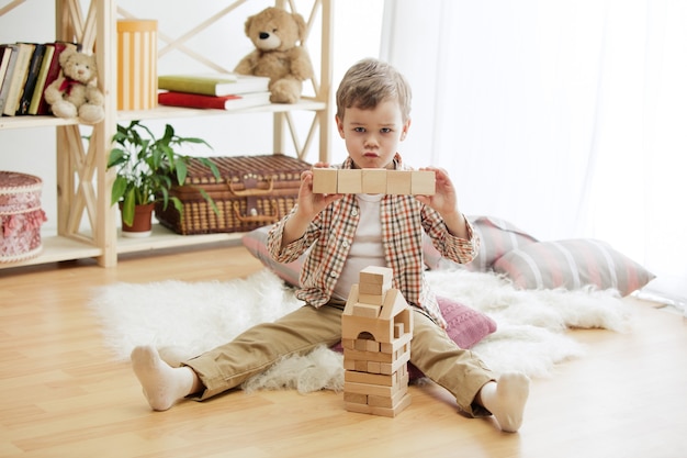 床に座っている小さな子供。家で木製の立方体を使ったかわいい男の子。テキストのコピーまたはネガティブ スペースとモックアップを含む概念的なイメージ