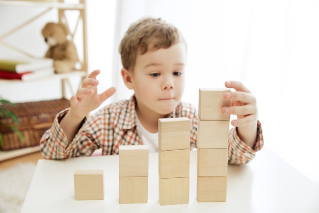 床に座っている小さな子供。家で木製の立方体で遊んでいるかわいい男の子。コピーまたはネガティブスペースのある概念的なイメージ