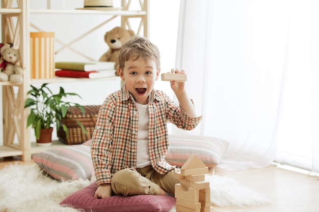 Foto gratuita piccolo bambino seduto sul pavimento. ragazzo sorpreso abbastanza sorridente che gioca con i cubi di legno a casa.