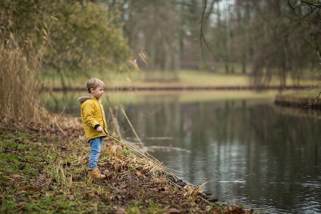 Little child trying to catch something with a long stick from a lake