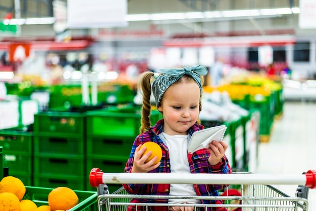 Little consumer making liste of products to buy while shopping in supermarket
