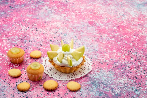 маленький кремовый торт с нарезанными фруктами печенье на цветном столе, торт сладкого цвета сахара