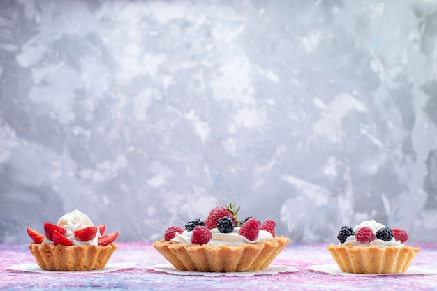 Foto gratuita piccole torte cremose con frutti di bosco su bianco chiaro, torta biscotto bacca dolce foto cuocere