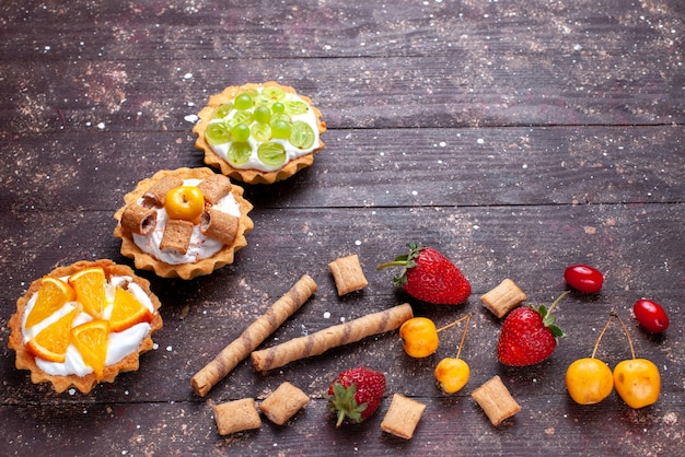 Piccole torte cremose con uva affettata arance insieme a fragole sulla scrivania in legno marrone, torta biscotto dolce di frutta