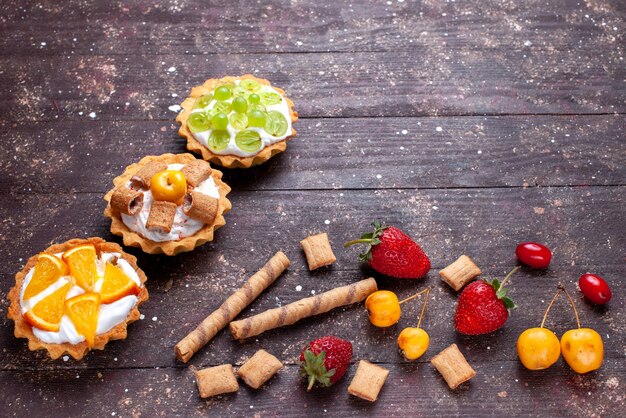маленькие сливочные пирожные с нарезанными виноградными апельсинами вместе с клубникой на коричневом деревянном столе, фруктовый бисквитный торт