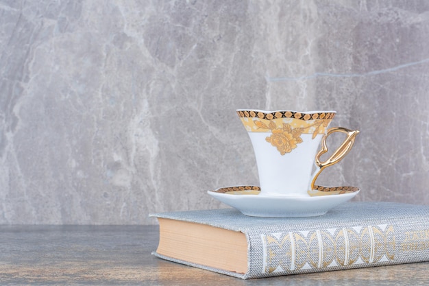 A little cup standing on book on marble background . High quality photo