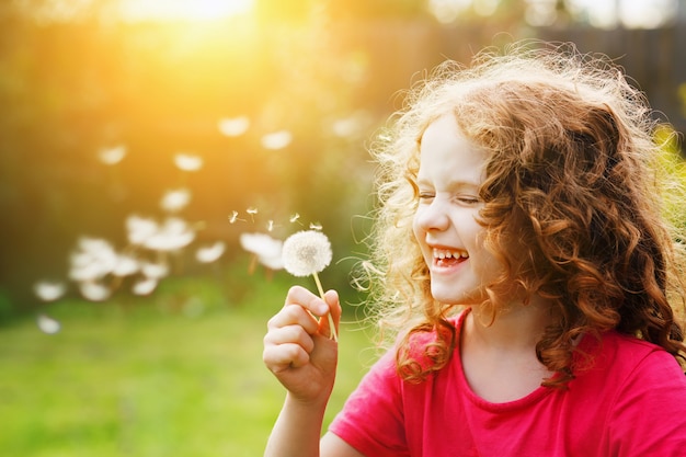 Little curly girl blowing dandelion and laughing.