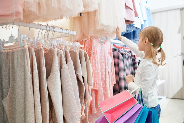 Little customer standing in store and choosing new dresses