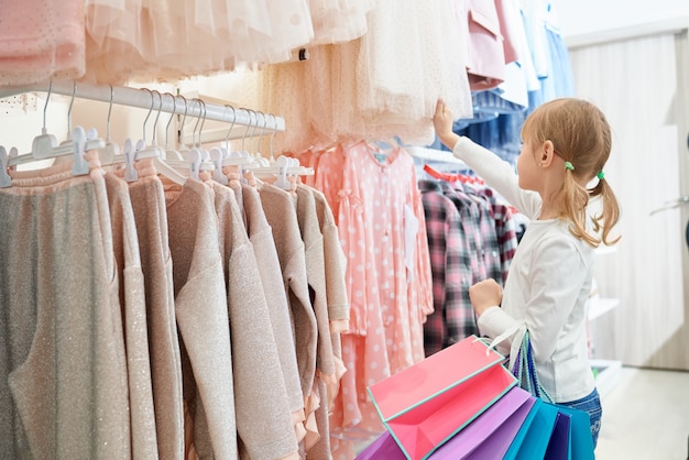 Little customer standing in store and choosing new dresses