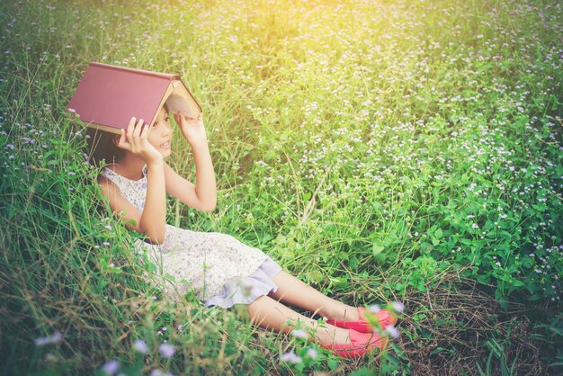 little cute asian girl cover book on her head at nature.