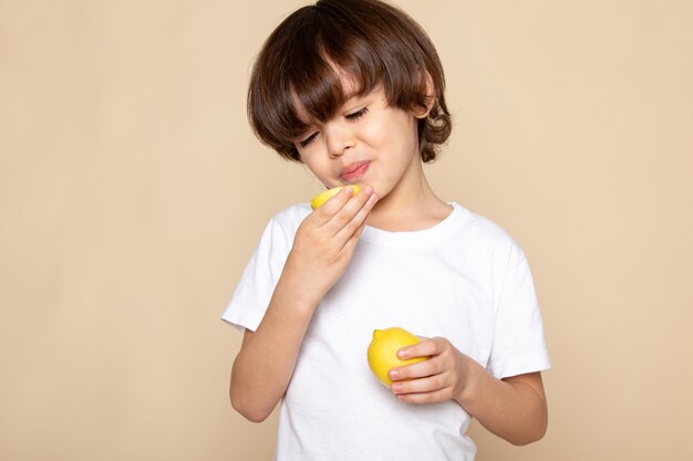 little cute boy eating sour lemon on pink