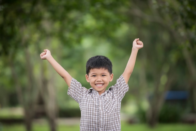 ぼんやりとした自然の背景上に自然と手をあげて楽しむ少しかわいい男の子。