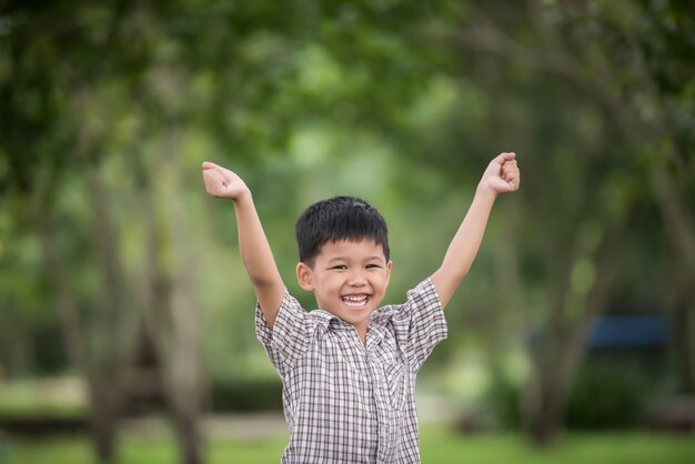 ぼんやりとした自然の背景上に自然と手をあげて楽しむ少しかわいい男の子。