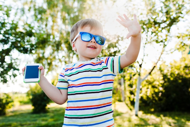 かわいい男の子がハイファイブをあげ、電話を手に持っています。