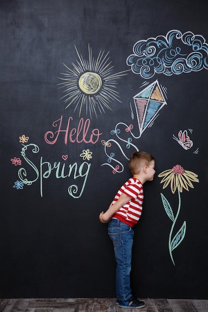 Little cute boy smelling flower on the chalk black board