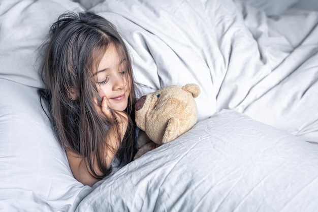 Little cute girl in bed with a teddy bear early in the morning copy space