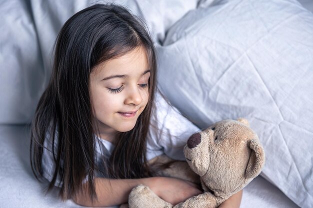 Little cute girl in bed with a teddy bear early in the morning