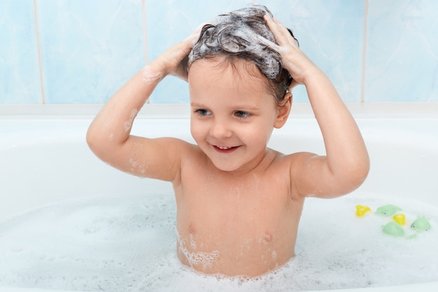 Little cute girl taking bath, washing her hair with shampoo