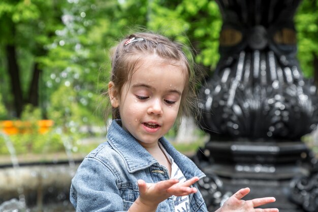 Little cute girl wets hands in the fountain