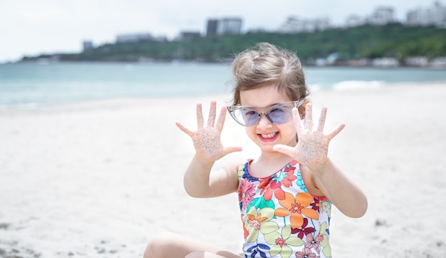 A little cute girl with glasses is playing in the sand on the beach by the sea.