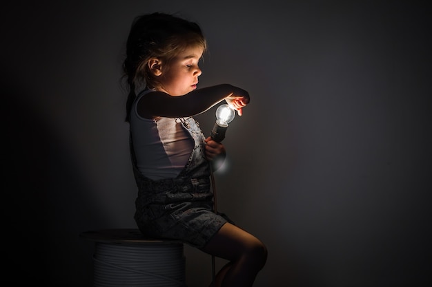 Free photo little cute girl with light bulb in hand sitting on the hank of wires for electricians,concept ideas