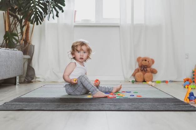 床​に​座って​おもちゃ​の​文字​で​遊ぶ​小さな​かわいい​幼児