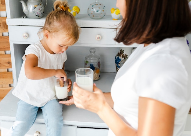 Little daughter eating cookies with milk