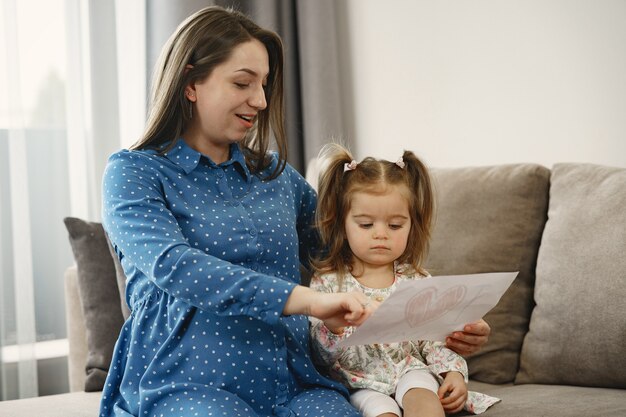 Little daughter with ponytails. Pregnant mom in a dress. Daughter with a picture.