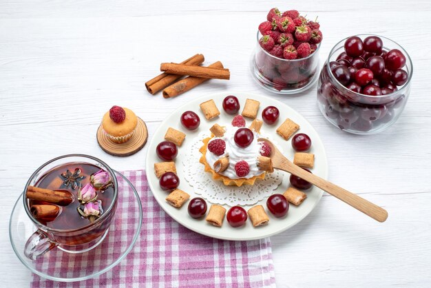 маленький вкусный торт с малиной, вишней и маленьким печеньем, чай с корицей на белом, фруктовый чай со сливками