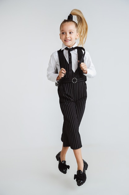 Little female caucasian model posing in school's uniform with backpack on white background.