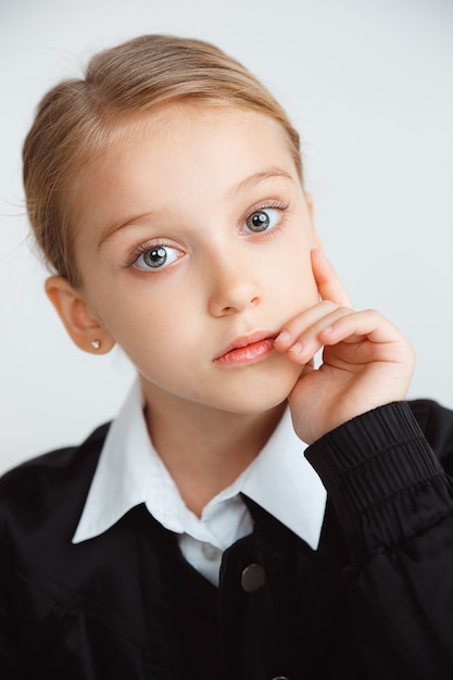 Little female model posing in school's uniform on white studio wall