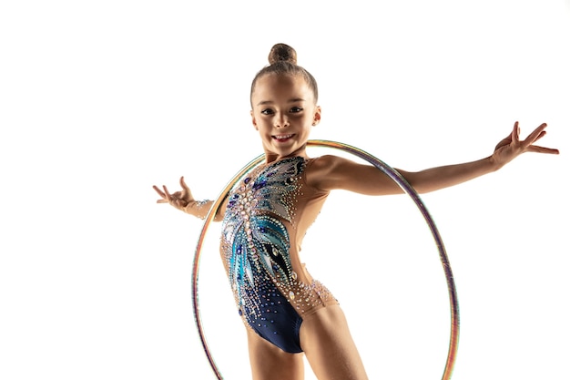 Little flexible girl isolated on white  wall. Little female model as a rhythmic gymnastics artist in bright leotard. Grace in motion, action and sport. Doing exercises with the hoop.