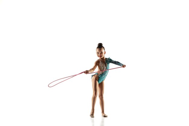 Little flexible girl isolated on white  wall. Little female model as a rhythmic gymnastics artist in bright leotard. Grace in motion, action and sport. Doing exercises with the jump rope.