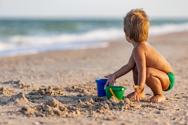 Маленький смешной забавный малыш, собирает ракушки и камешки в спокойном синем море на песчаном дне под жарким летним солнцем в ярком отпуске