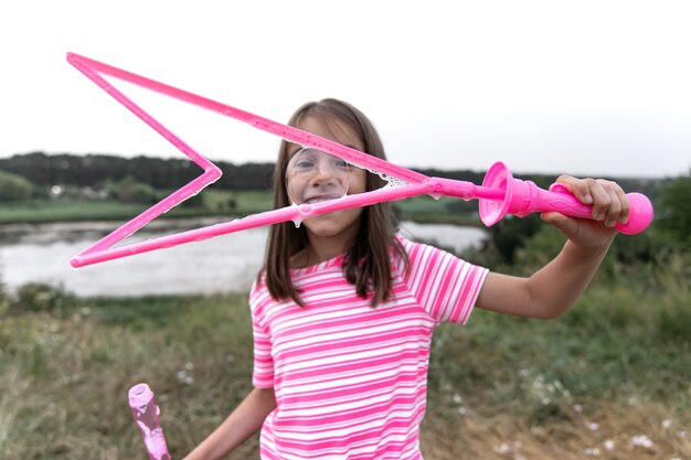 A little funny girl blows soap bubbles in the summer in a field, outdoor summer activities.