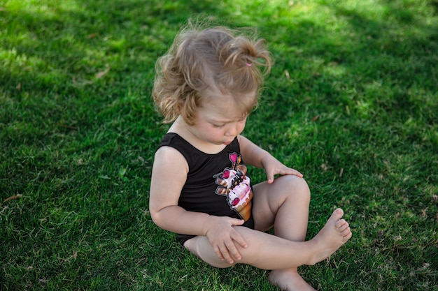 Маленькая забавная девочка летом сидит на траве в саду