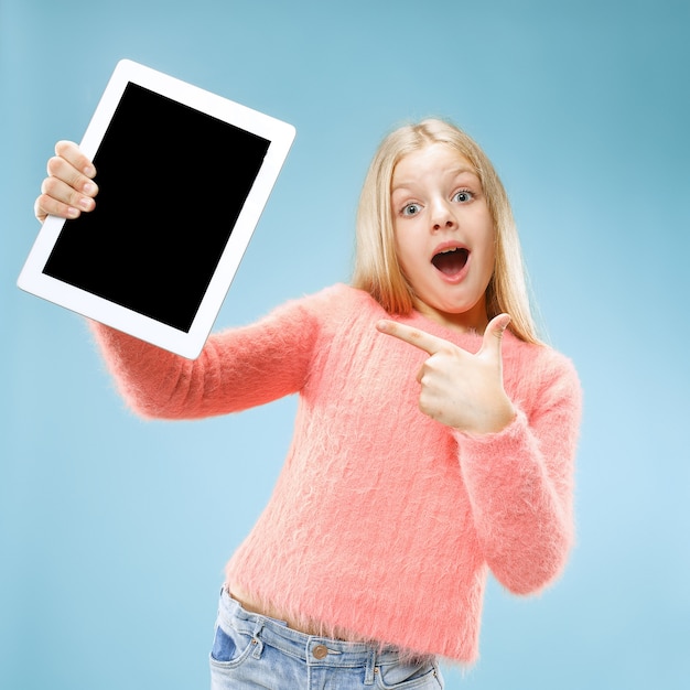 Free photo little funny girl with tablet on blue studio. she showing something and pointing at screen.