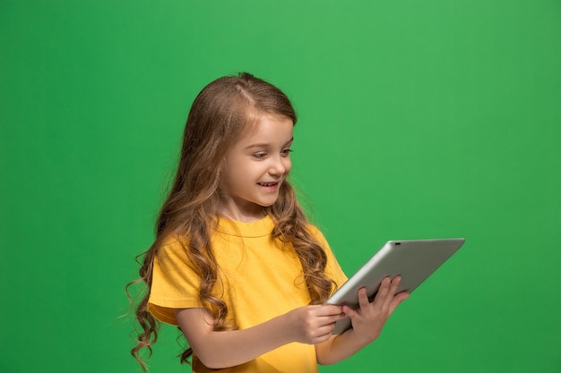 Free photo little funny girl with tablet on green studio background. she showing something and looking at screen.