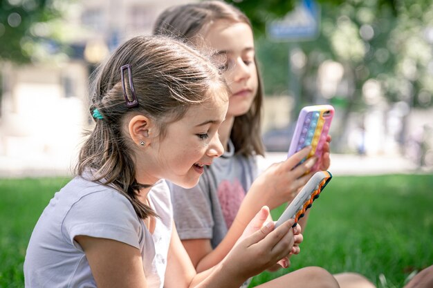 にきびのあるケースに携帯電話を持っている屋外の小さな面白い女の子がそれをポップします、流行の抗ストレスおもちゃ。