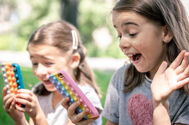 Маленькие веселые девчонки на природе с телефонами в чехле от прыщей - это модная антистрессовая игрушка.