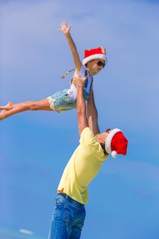 해변 휴가 동안 산타 모자에 어린 소녀와 행복한 아빠