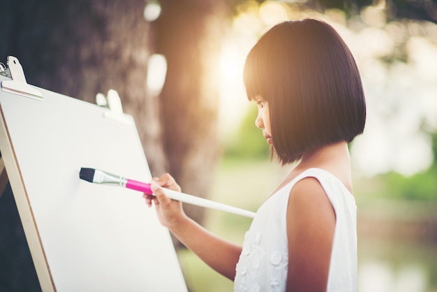 Free photo little girl artist painting picture in the park