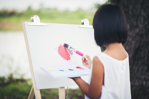 Free photo little girl artist painting picture in the park