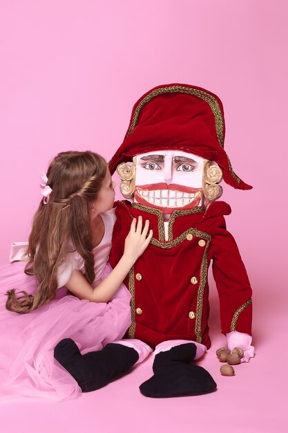 A little girl as beauty ballerina at pink long dress with nutcracker at pink studio