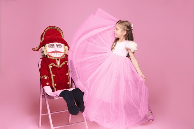 Маленькая девочка как балерина в розовом длинном платье с щелкунчиком в розовой студии