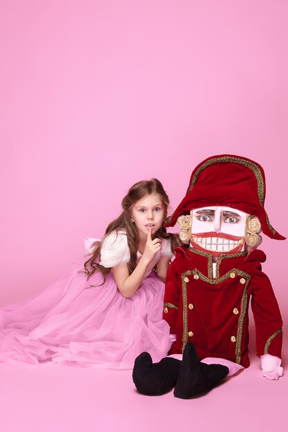 A little girl as beauty ballerina at pink long dress with nutcracker at pink studio