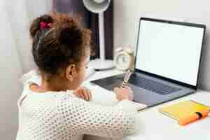 Free photo little girl attending online school at home using laptop